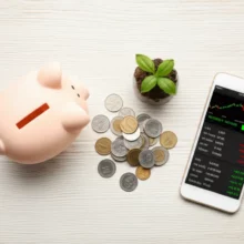 스마트폰-주식-앱-화면,-돼지-저금통,-동전,-새싹이-나무-배경-위에-놓여-중개형-ISA-인기를-상징하는-이미지