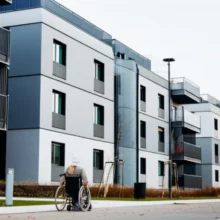A-person-in-a-wheelchair-looking-towards-modern-apartment-buildings,-symbolizing-hope-for-accessible-housing.