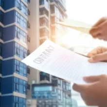 Hands-exchanging-documents-related-to-apartment-ownership-transfer-with-an-apartment-building-in-the-background.