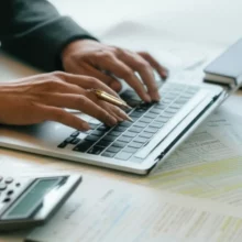 Hands-typing-on-a-laptop-surrounded-by-tax-documents-and-a-calculator,-symbolizing-online-tax-reporting.