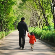 A-parent-and-child-walk-hand-in-hand-on-a-quiet,-shaded-forest-path-in-Seoul.