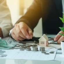 Hands-arranging-money,-a-model-house,-and-a-plant-on-a-desk,-symbolizing-holistic-retirement-planning.