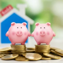 부부-공동명의-양도세-절세-현명한-선택을-상징하는-두-개의-귀여운-저금통이-손을-잡고-있고,-뒤로는-부동산과-동전이-보여-재테크와-세금-절감-효과를-표현하는-이미지