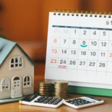작고-귀여운-집-모형과-계산기,-달력이-놓인-탁자-이미지.-부동산-재산세-계산-방법과-납부-일정을-나타내는-그림입니다.